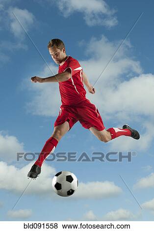 Stock Photo - Soccer player jumping in mid-air kicking ball. Fotosearch