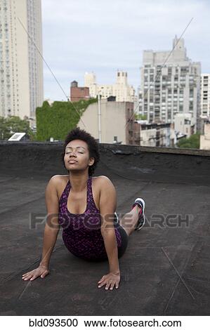 Stock Image - African American woman practicing yoga on rooftop. Fotosearch