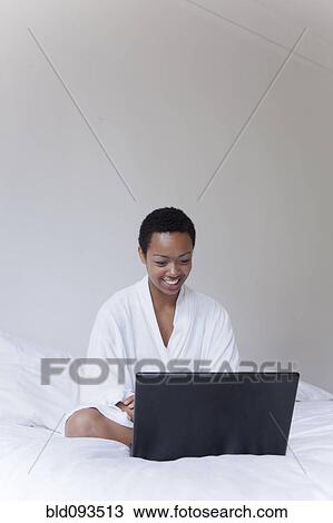 Stock Image - African American woman using laptop in bed. Fotosearch
