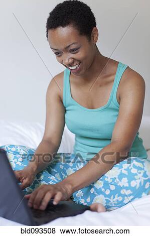 Stock Photo - African American woman using laptop in bed. Fotosearch