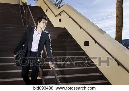 Stock Image - Asian businessman descending staircase. Fotosearch