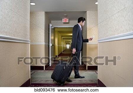 Stock Photograph - Asian businessman pulling suitcase in hotel. Fotosearch