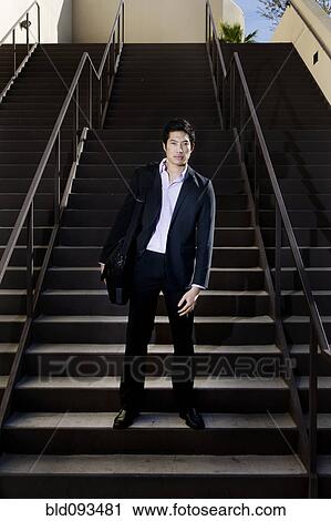 Stock Image - Asian businessman standing on staircase. Fotosearch