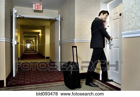 Stock Photo - Asian businessman using cell phone and entering hotel room. Fotosearch