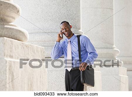 Stock Image - Black businessman talking on cell phone outdoors. Fotosearch