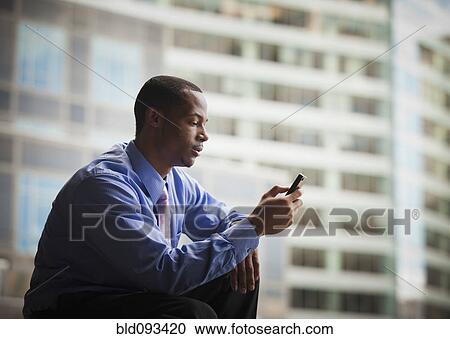 Stock Image - Black businessman text messaging on cell phone. Fotosearch