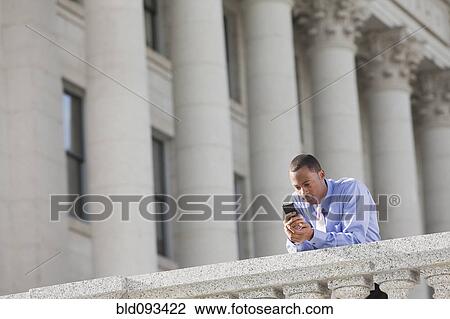 Stock Image - Black businessman text messaging on cell phone. Fotosearch