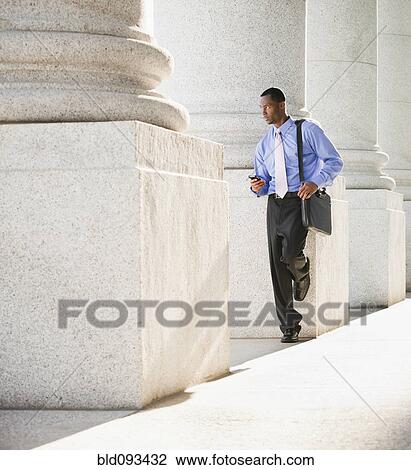Stock Image - Black businessman text messaging on cell phone outdoors. Fotosearch