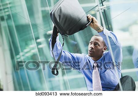 Stock Image - Black businessman turning briefcase upside-down looking for something. Fotosearch