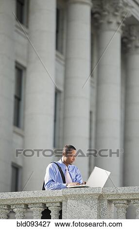 Stock Photo - Black businessman using laptop outdoors. Fotosearch