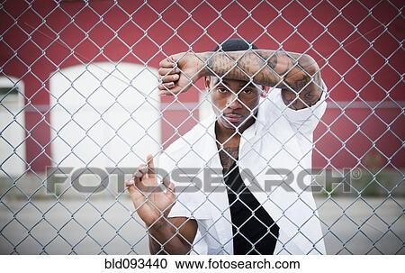 Stock Image - Black man leaning on chain link fence. Fotosearch