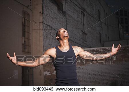 Stock Image - Black man standing outdoors with arms outstretched. Fotosearch