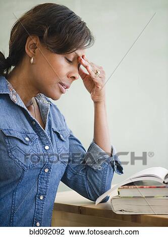 Stock Image - Black teacher in classroom with headache. Fotosearch
