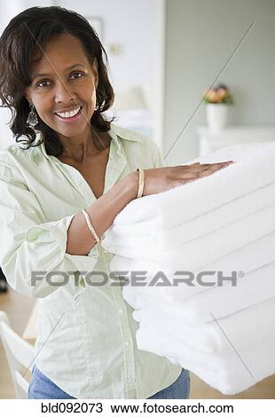 Stock Image - Black woman carrying stack of towels. Fotosearch