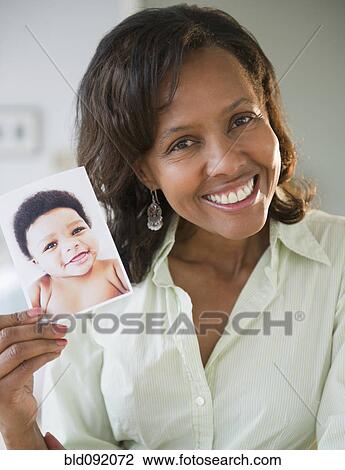 Stock Image - Black woman holding photograph of baby. Fotosearch