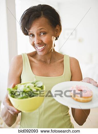 Stock Image - Black woman holding salad and donut. Fotosearch