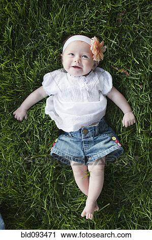 Stock Image - Caucasian baby girl laying in grass. Fotosearch