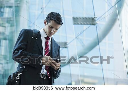 Stock Photograph - Caucasian businessman text messaging on cell phone outdoors. Fotosearch