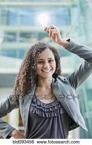 Stock Photograph - Caucasian businesswoman holding glowing light bulb over her head. Fotosearch