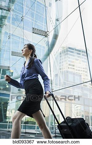 Stock Photo - Caucasian businesswoman pulling suitcase outdoors. Fotosearch