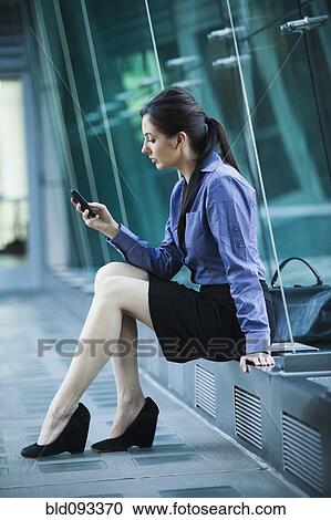 Stock Image - Caucasian businesswoman sitting outdoors using cell phone. Fotosearch