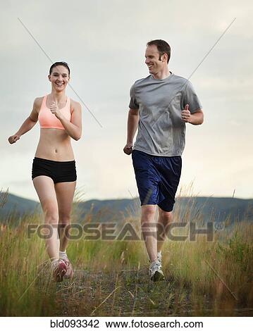 Stock Image - Caucasian couple running together on remote path. Fotosearch