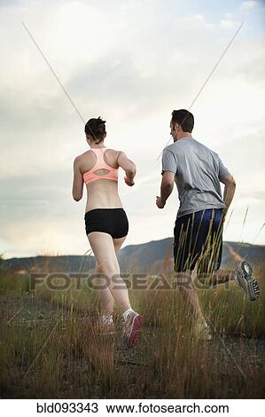 Stock Image - Caucasian couple running together on remote path. Fotosearch