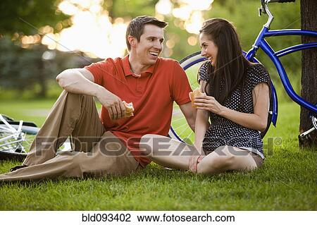 Stock Image - Caucasian couple sitting in grass eating lunch. Fotosearch