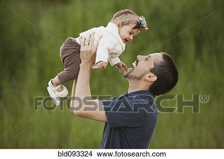 Picture - Caucasian father lifting daughter outdoors. Fotosearch