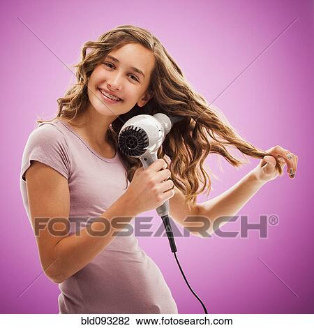 Stock Image - Caucasian teenager blow drying her hair. Fotosearch