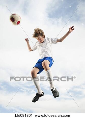 Stock Image - Caucasian teenager heading soccer ball in mid-air. Fotosearch