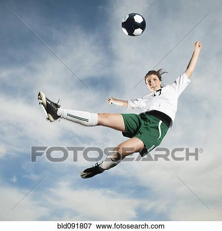 Stock Photo - Caucasian teenager kicking soccer ball in mid-air. Fotosearch