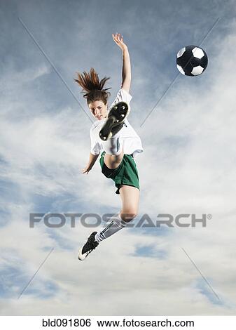 Stock Photograph - Caucasian teenager kicking soccer ball in mid-air. Fotosearch