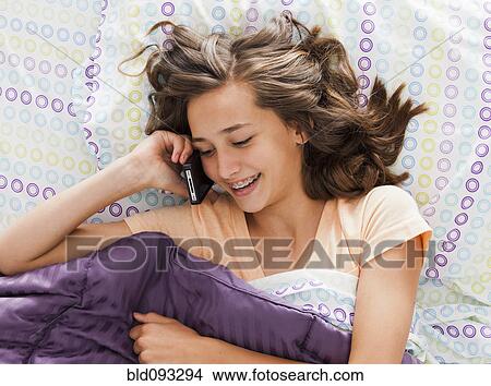 Picture - Caucasian teenager laying in bed talking on cell phone. Fotosearch