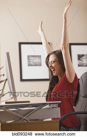 Caucasian woman cheering at desk in home office View Large Photo Image Stock Photo - Caucasian woman cheering at desk in home office. Fotosearch