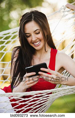 Stock Image - Caucasian woman in hammock text messaging on cell phone. Fotosearch
