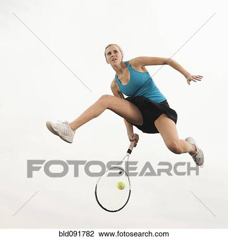 Stock Image - Caucasian woman jumping in mid-air playing tennis. Fotosearch