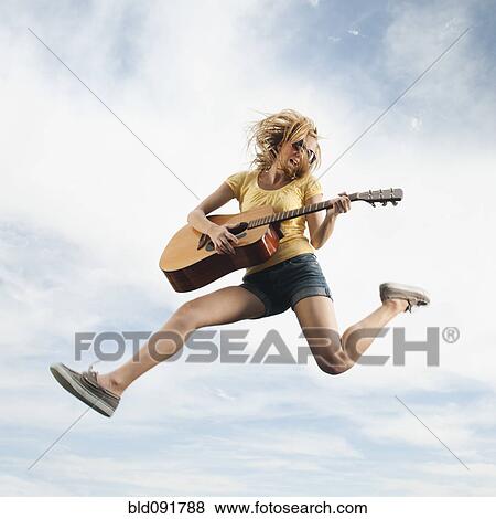 Stock Photo - Caucasian woman jumping in mid-air playing guitar. Fotosearch