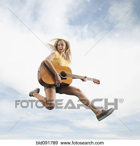 Stock Photo - Caucasian woman jumping in mid-air playing guitar. Fotosearch