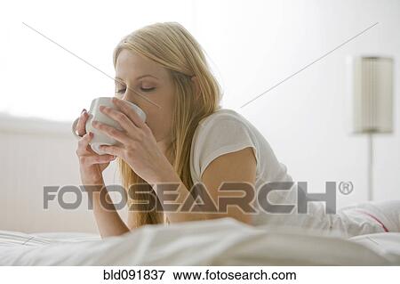 Stock Photo - Caucasian woman laying in bed drinking coffee. Fotosearch