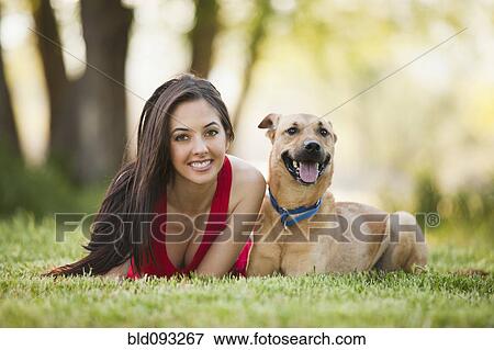 Stock Photo - Caucasian woman laying in grass with dog. Fotosearch