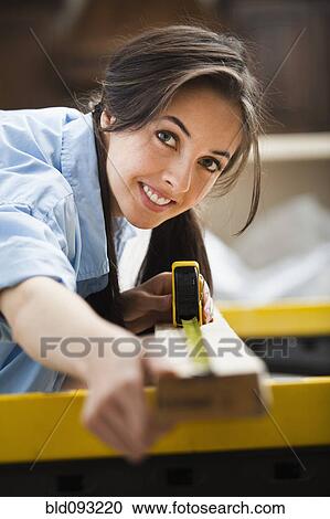 Stock Image - Caucasian woman measuring wood. Fotosearch