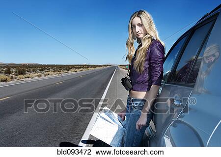 Stock Image - Caucasian woman reading map at roadside. Fotosearch