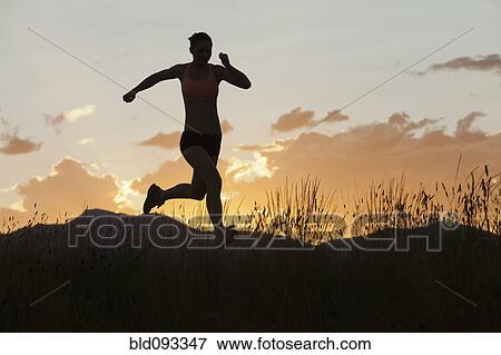 Stock Photo - Caucasian woman running in remote area at sunset. Fotosearch