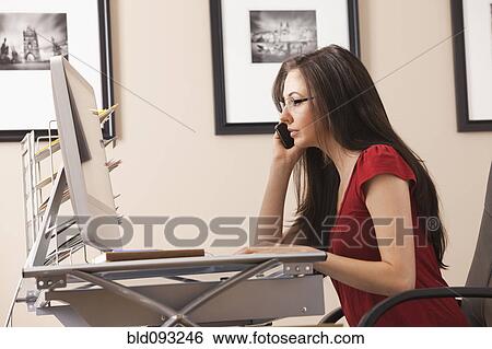 Stock Photograph - Caucasian woman talking on phone at desk in home office. Fotosearch