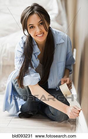 Stock Image - Caucasian woman taping wall. Fotosearch