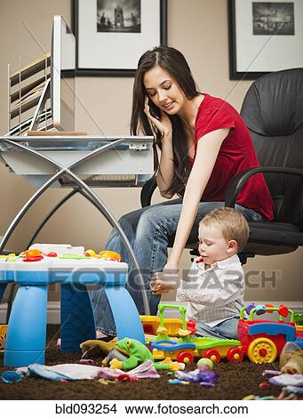 Picture - Caucasian woman tending child and working in home office. Fotosearch