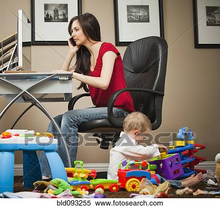 Stock Photography - Caucasian woman tending child and working in home office. Fotosearch
