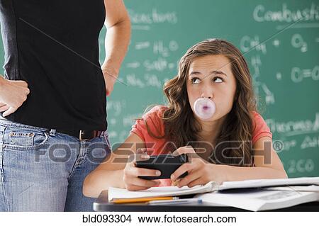 Picture - Frustrated teacher watching student with cell phone and gum. Fotosearch