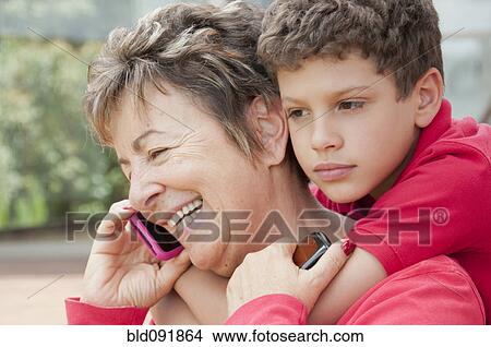 Picture - Hispanic boy hugging grandmother talking on cell phone. Fotosearch